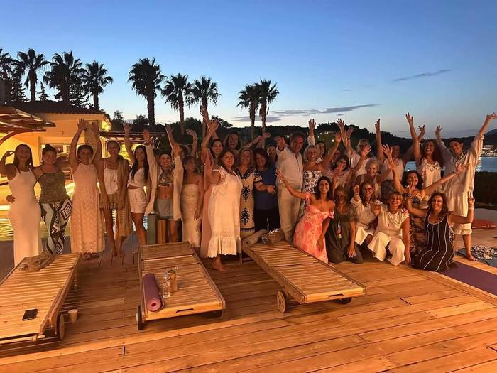 Group of people attending a healing retreat in Greece with palm trees and sunset in the background – AnaGennisi Academy seminars & retreats