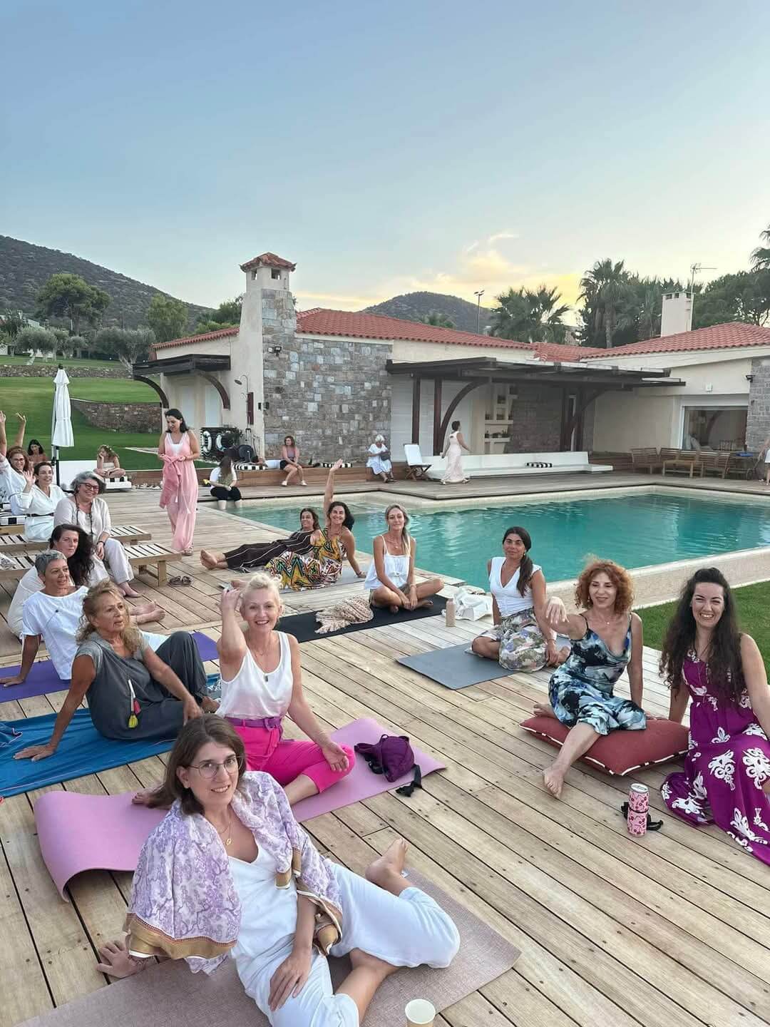 Group of women sitting on yoga mats by a poolside with a scenic background, seminar Embryogenesis in villa Athens , Anagennisi Academy