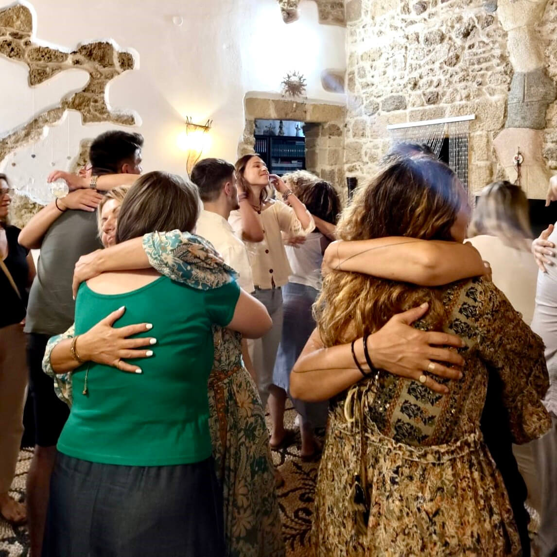 Systemic Soul Healing. People embracing in a lively indoor setting with stone walls and warm lighting.